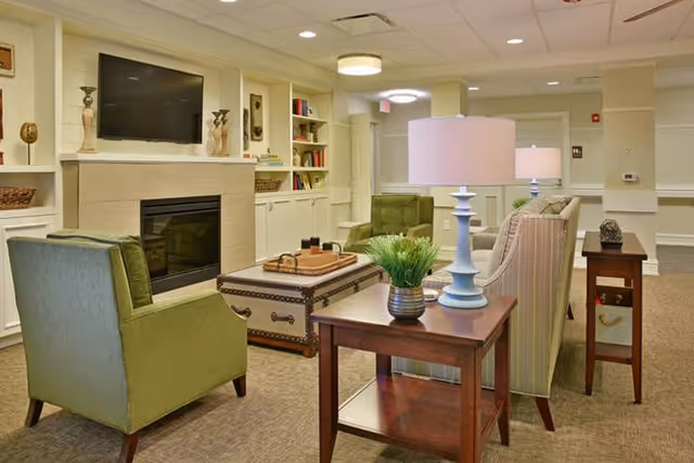 Cozy senior living common room with sofas, armchairs, a coffee table, fireplace, built-in shelves, and lamps.