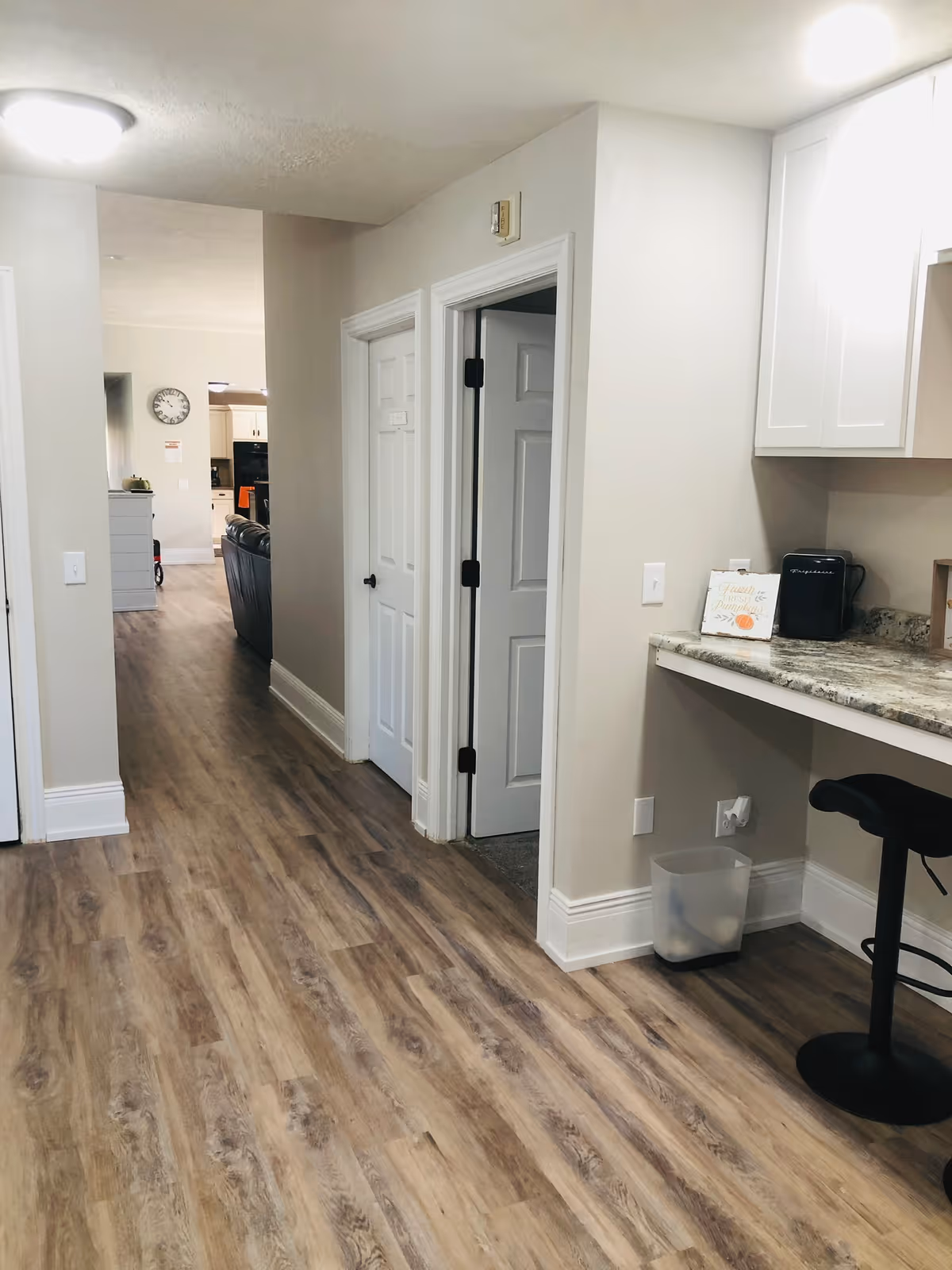 Interior hallway with wood-look flooring, two closed doors, a countertop with a bar stool, and a view into a living area/kitchen.