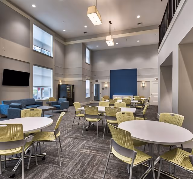 Bright senior living interior with round white tables, yellow chairs, and blue accent wall.