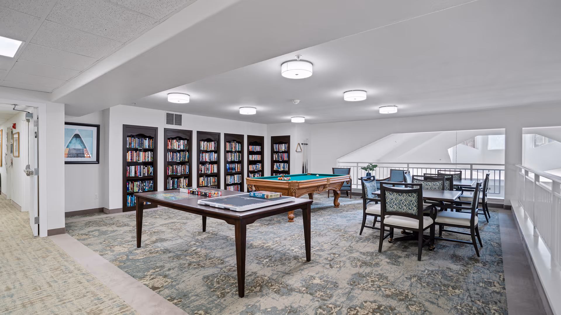 Open community activity room with a pool table, game table, bookshelves, and several seating/dining tables.