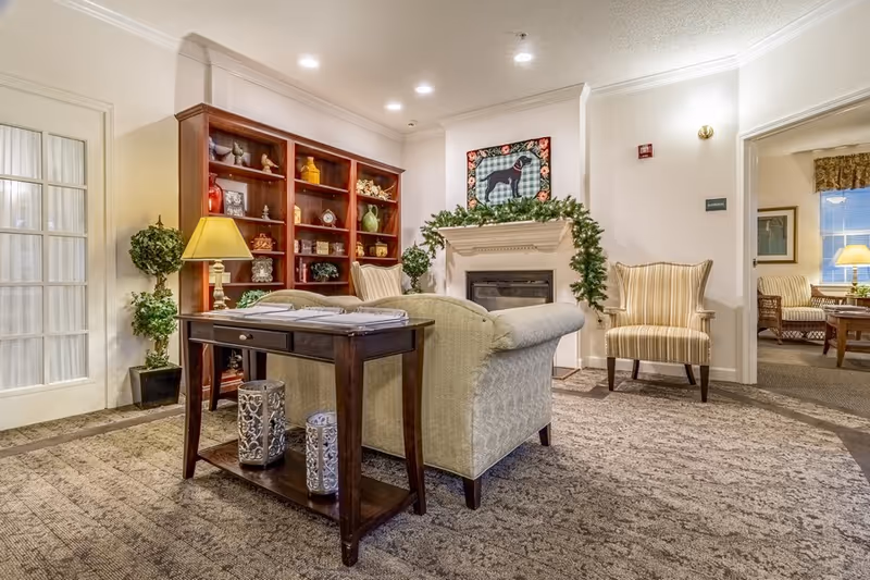Well-lit furnished lounge with a sofa, armchairs, a fireplace, built-in bookshelf and side table.
