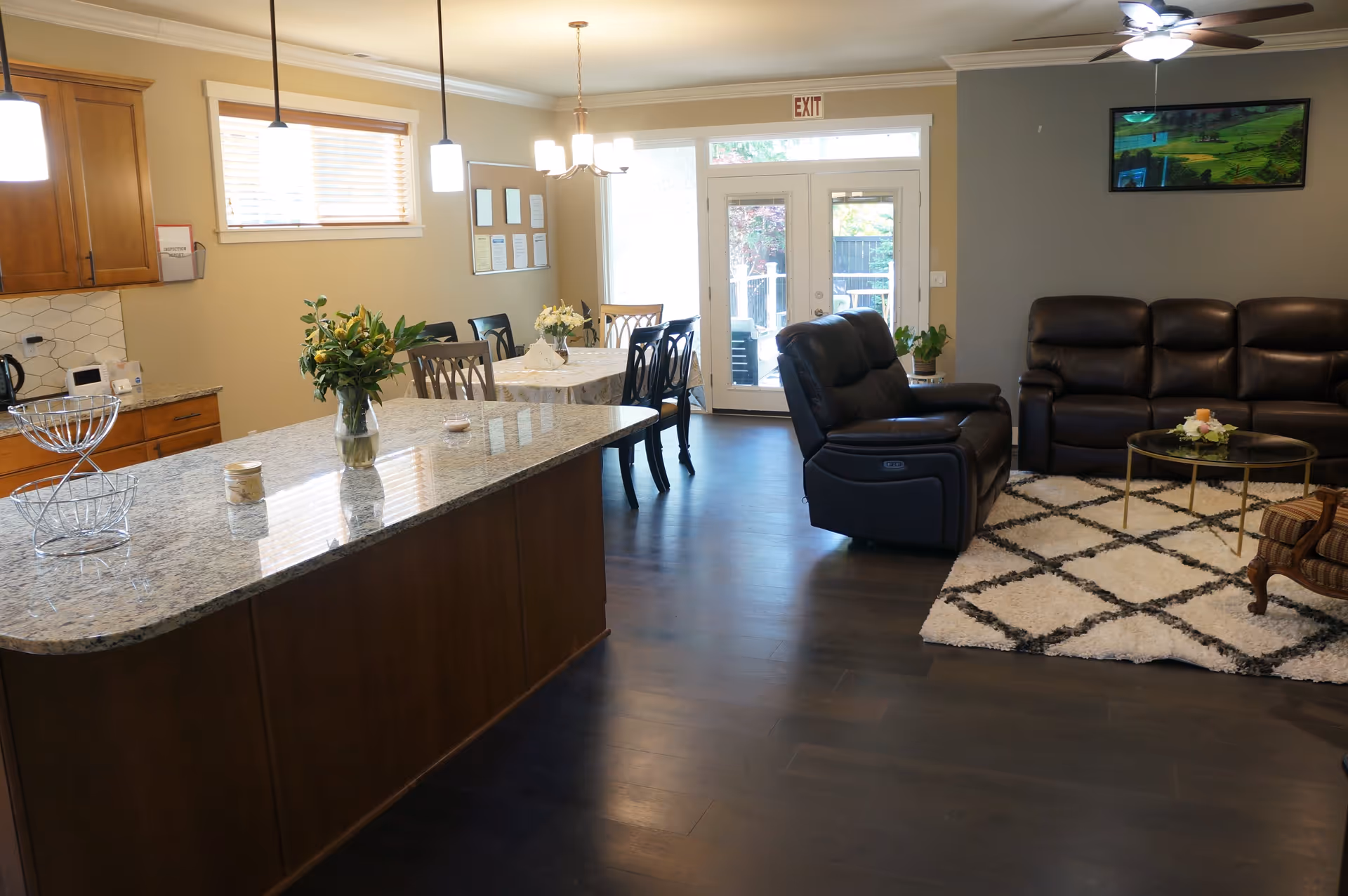 Open-plan living area with a kitchen island, dining table, and leather sofas facing a TV and glass doors.