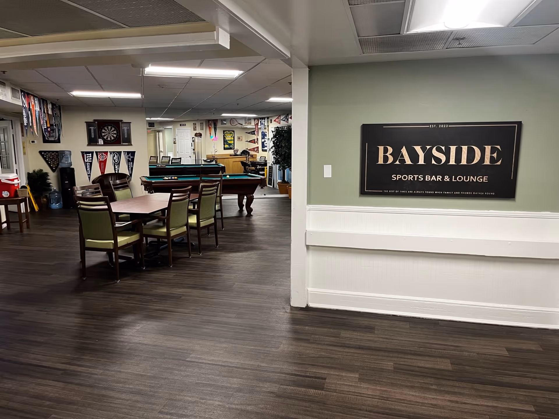 Community lounge with tables and chairs, pool tables and games, and a wall sign reading "BAYSIDE Sports Bar & Lounge".
