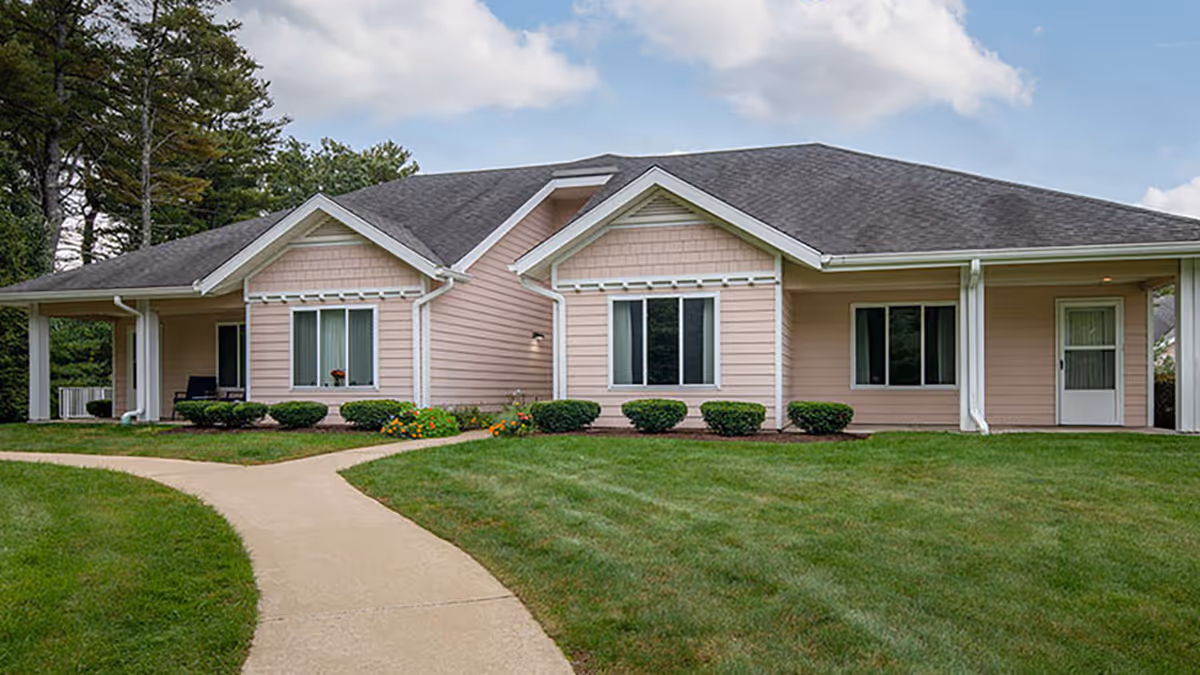 Front exterior of a single-story pink building with a curved walkway, lawn, shrubs, and windows.