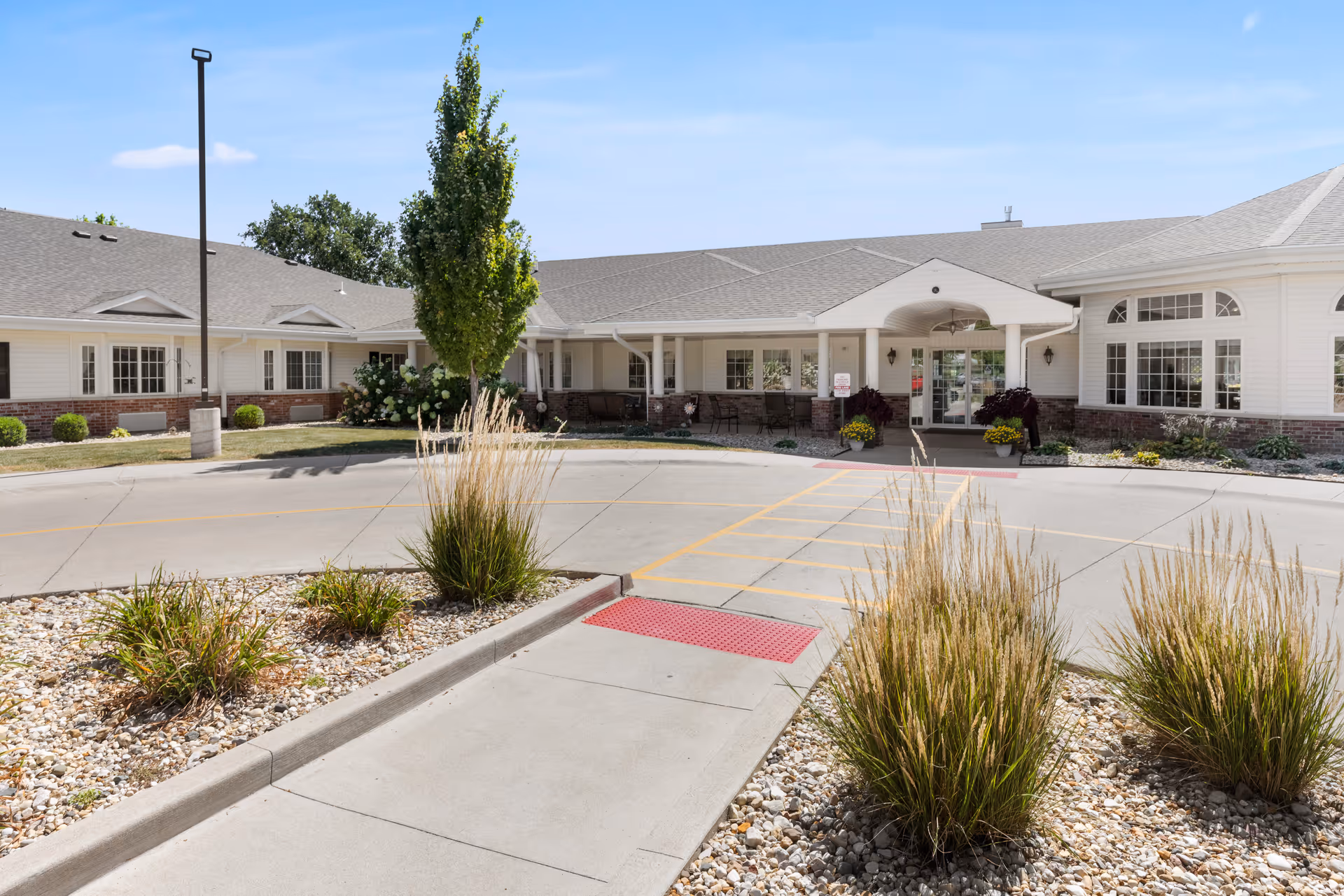Front entrance of a senior living facility with a covered porte-cochère, circular driveway, and landscaped rock beds.