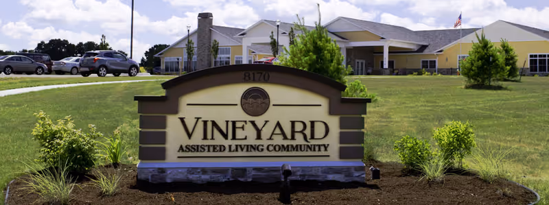 Sign for Vineyard Assisted Living Community with a landscaped area in front and a building in the background.