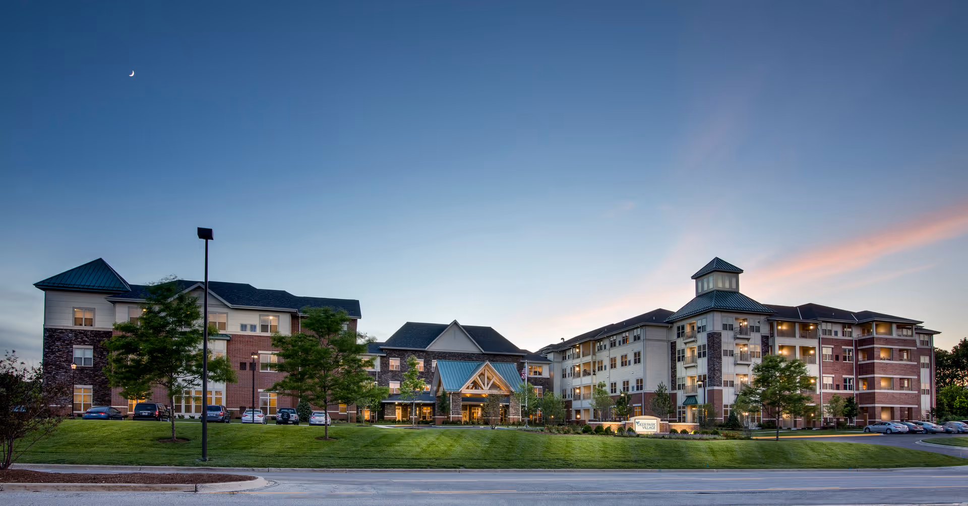 Wide exterior view of a multi-story senior living facility at dusk with a manicured lawn and main entrance.