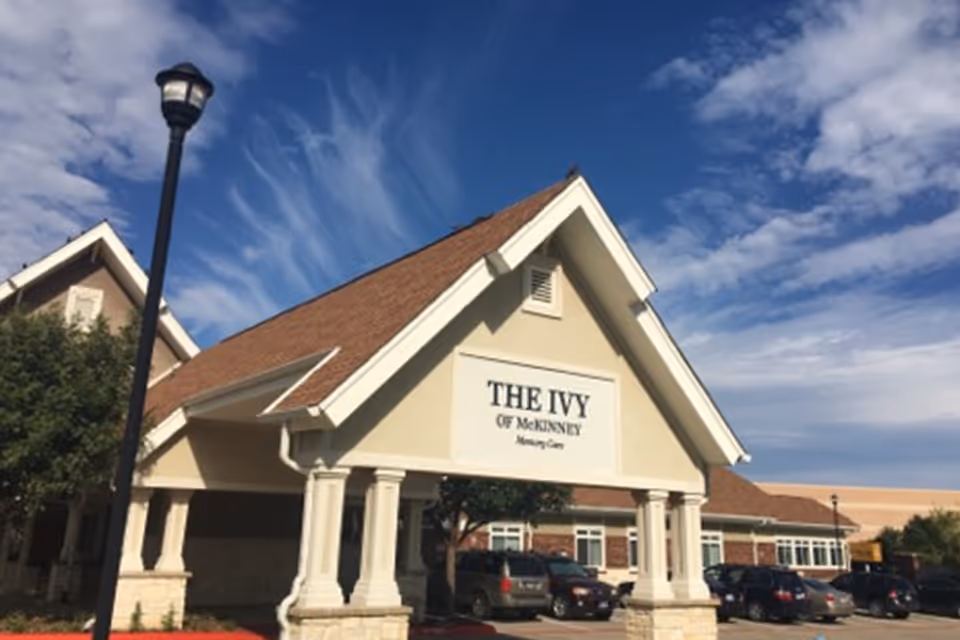 Front view of The Ivy of McKinney facility with parked cars and clear sky