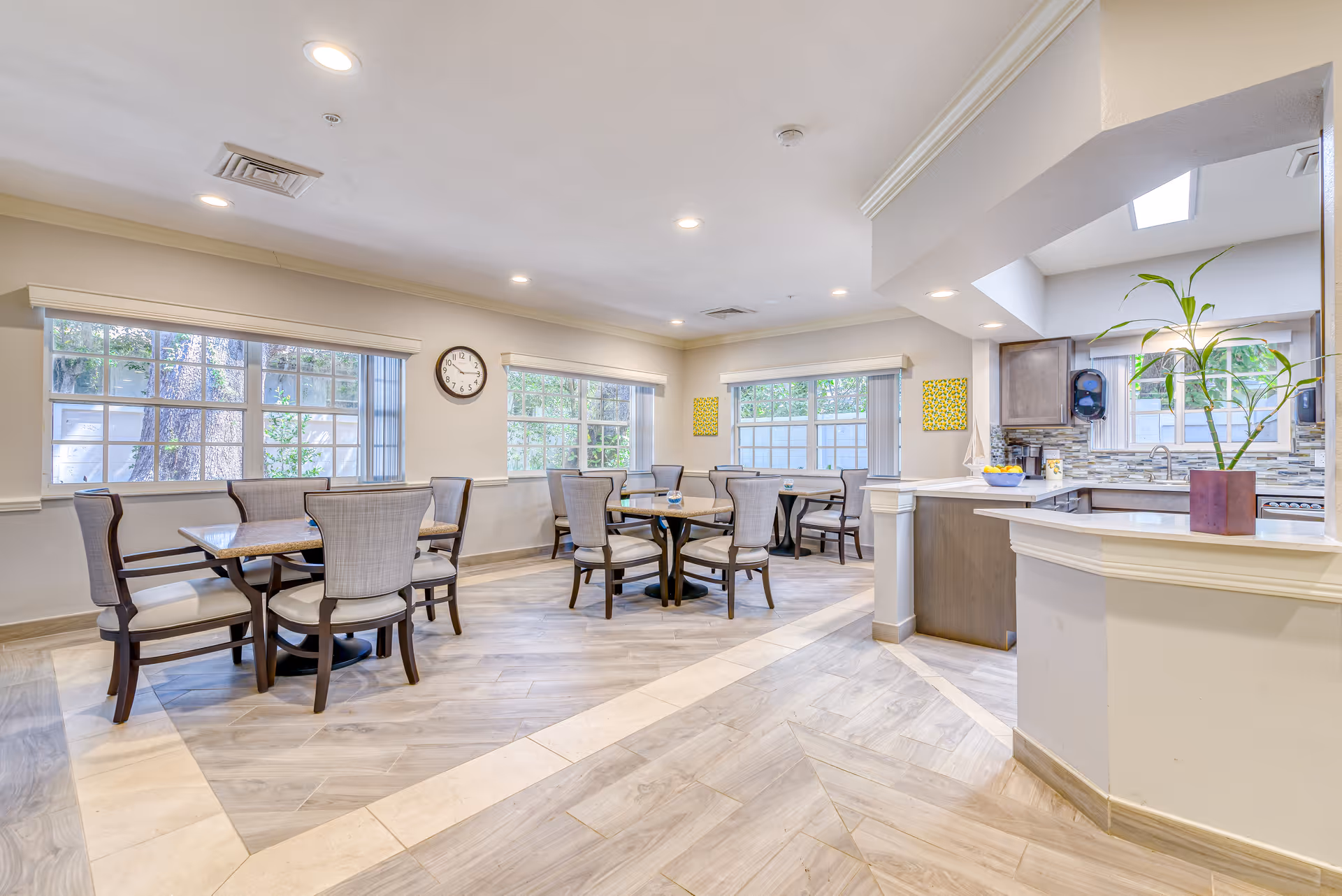 Bright communal dining area with several tables and chairs next to a service counter and kitchen.
