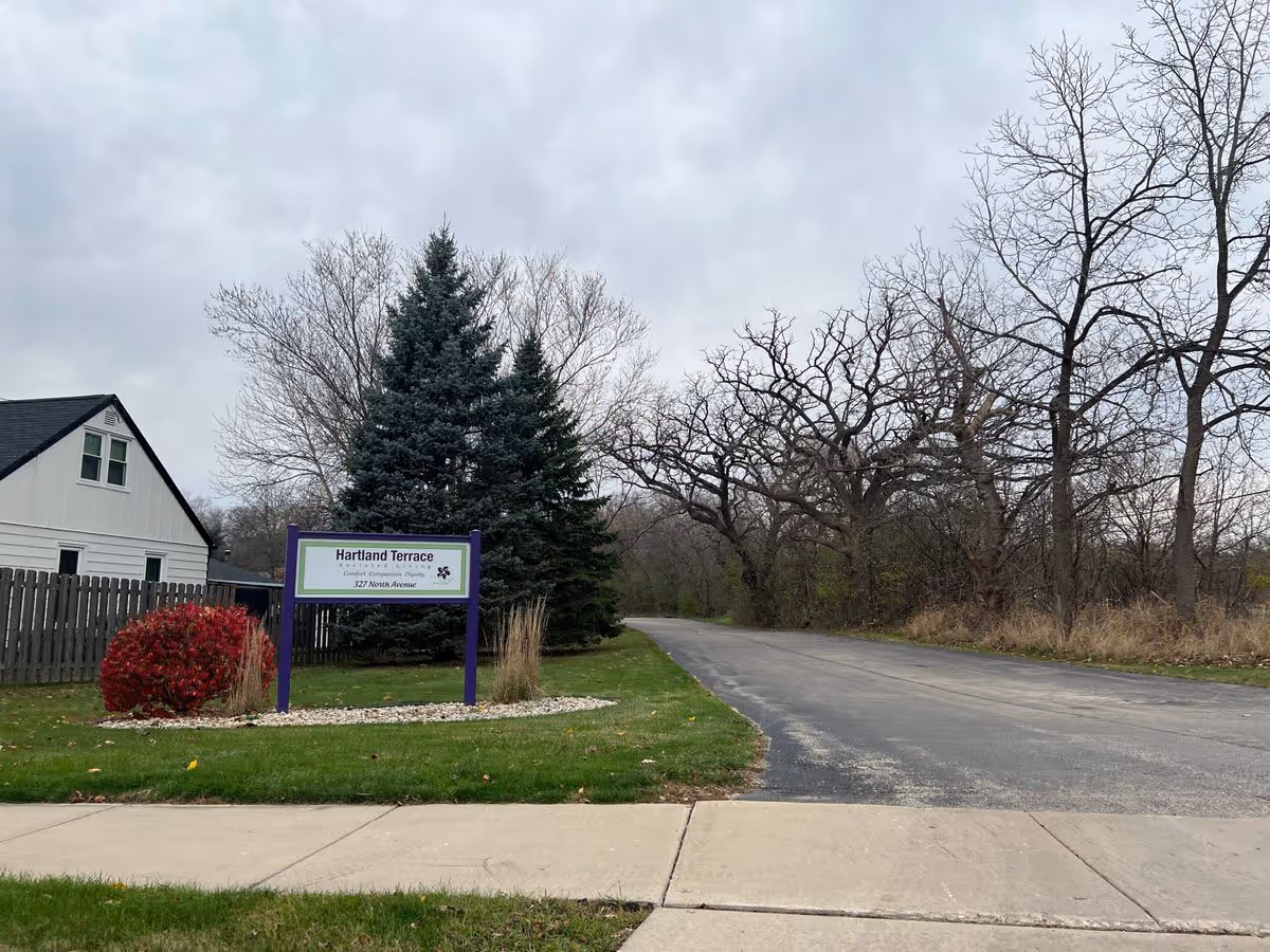 Entrance sign for Hartland Terrace by a driveway with lawn, trees, and a cloudy sky.