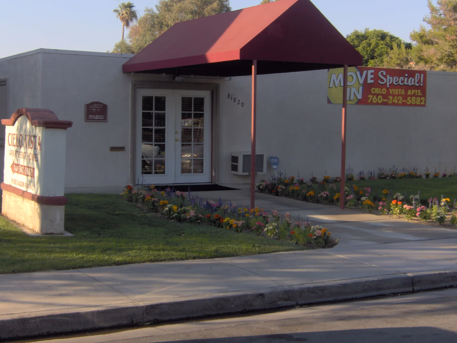 Entrance to Cielo Vista Apartments with a red awning, double doors, landscaped flower beds, and signage.