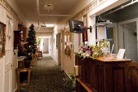 Narrow hallway inside a senior living facility with a reception desk, plants, and holiday decorations.