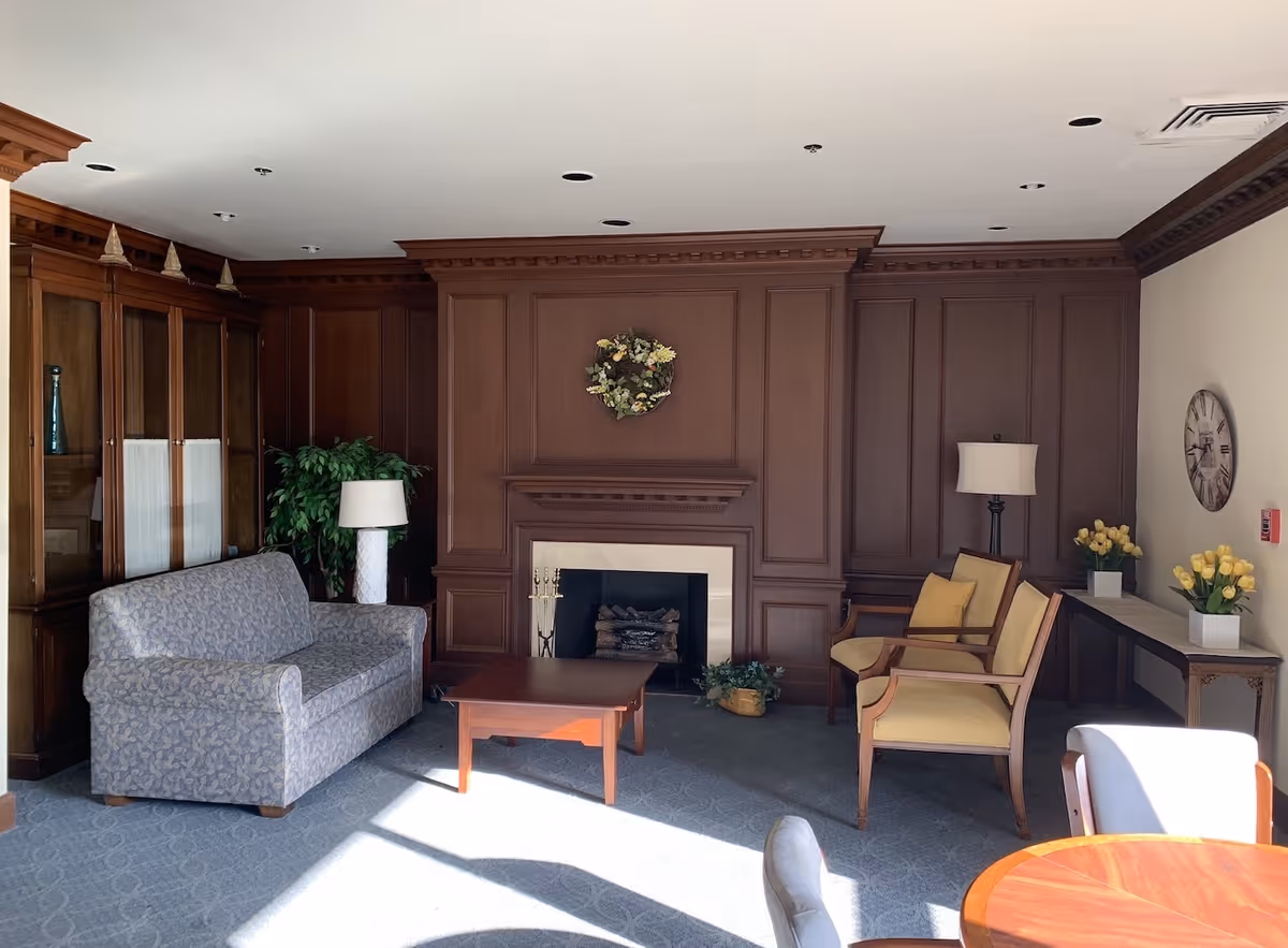 Wood-paneled common living room with a fireplace, sofa, armchairs, coffee table and lamps.