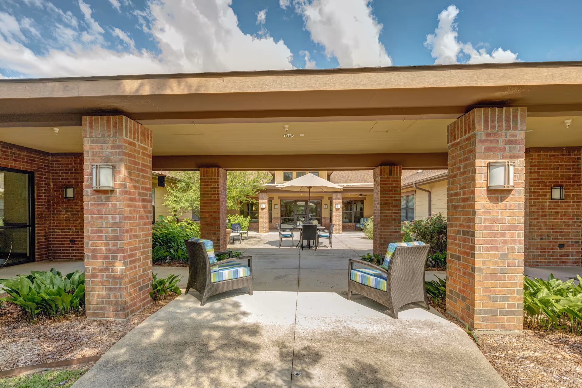 Covered brick entrance courtyard with wicker chairs, columns, and an outdoor seating area with an umbrella.