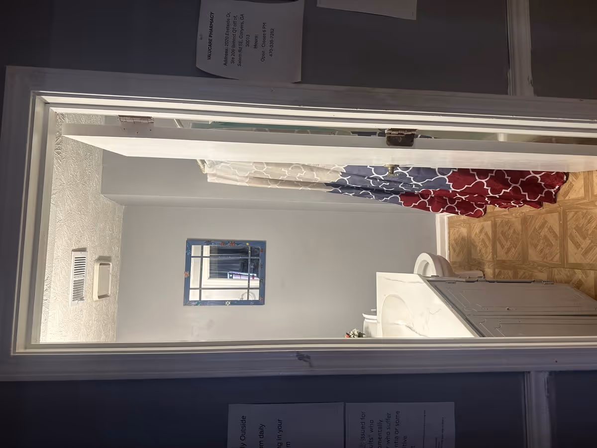 View through an open doorway into a bathroom with a vanity sink, toilet, and a red-and-blue patterned shower curtain.