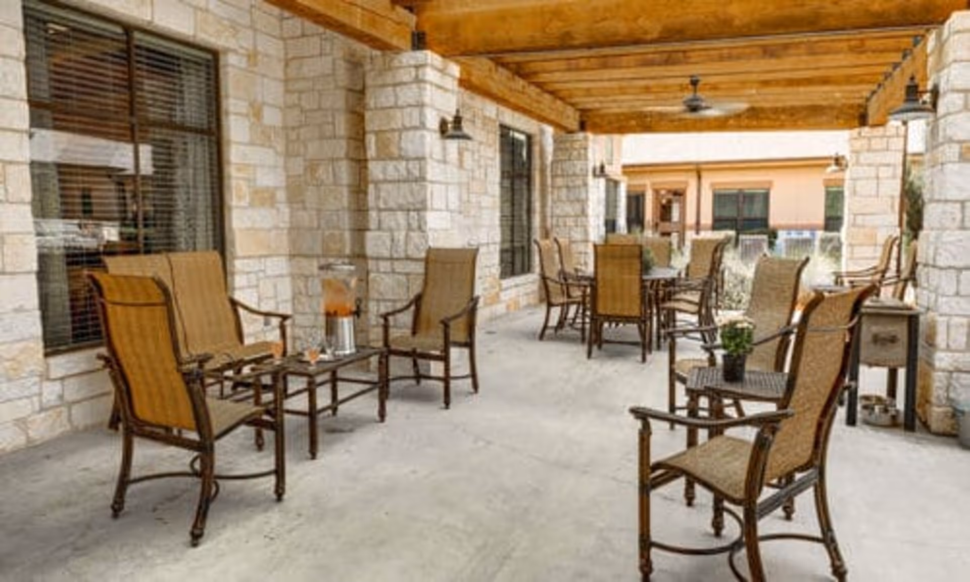 Covered stone patio with multiple wicker-style chairs and tables arranged for outdoor seating.