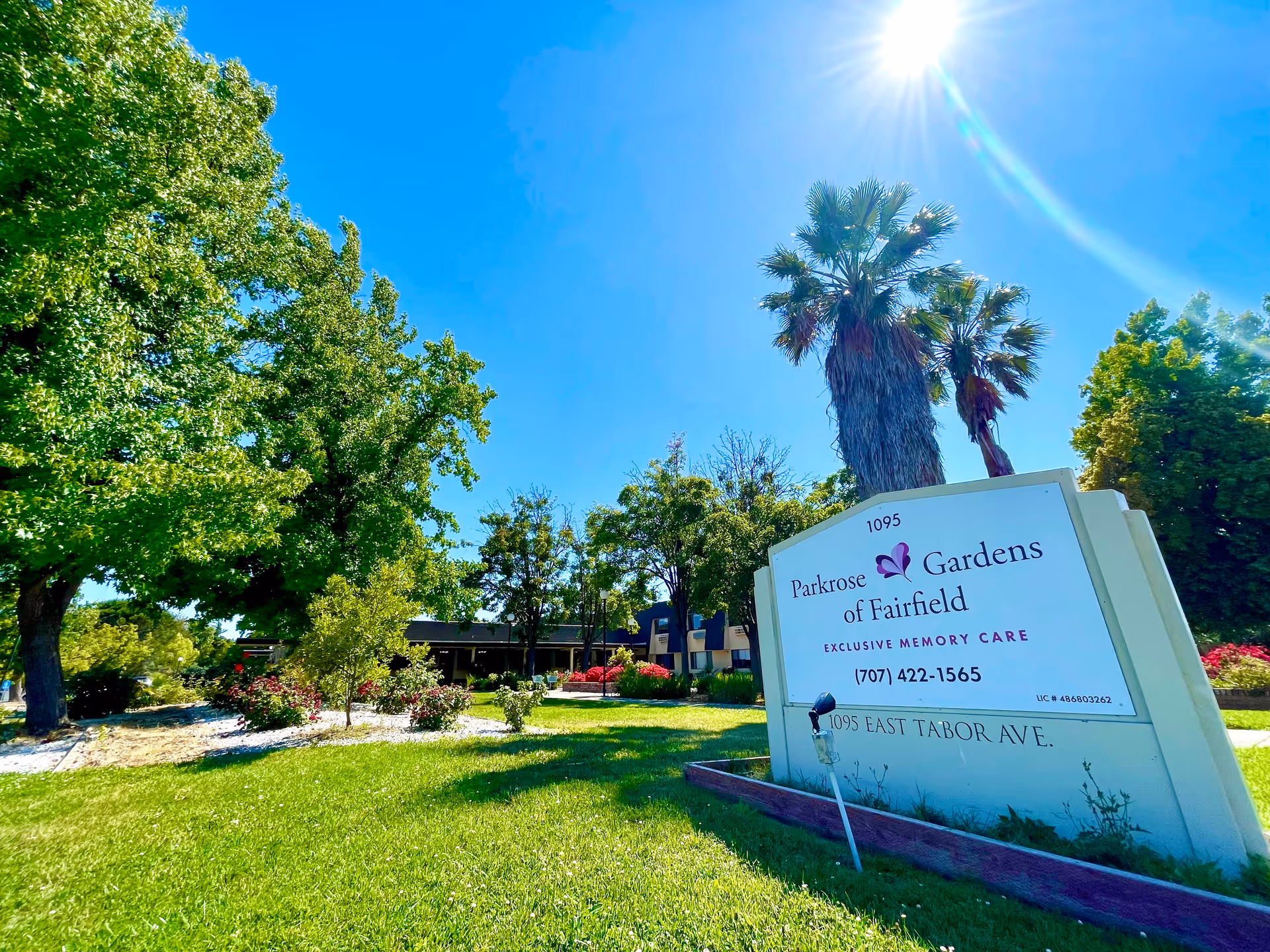 Outdoor view of Parkrose Gardens of Fairfield facility sign with trees, green grass, and a clear blue sky with sunlight.