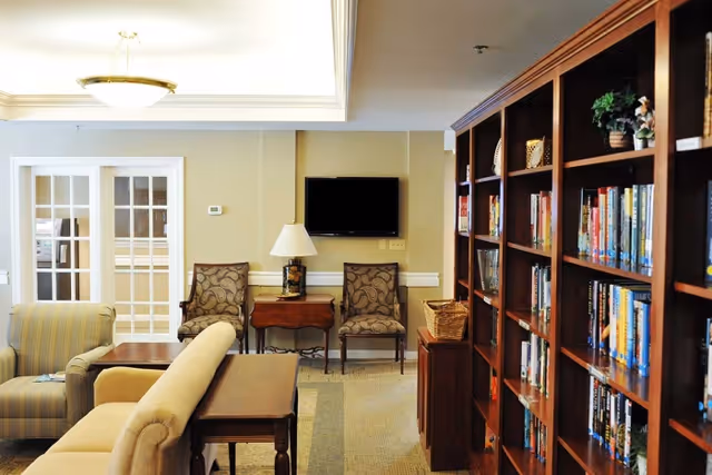 Cozy common room with bookshelves along the right wall, sofas and chairs facing a wall-mounted TV.