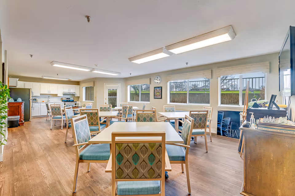 Bright communal dining area with multiple tables and patterned chairs and an open kitchenette in the background.