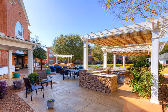 Outdoor courtyard with pergolas, seating areas, and an outdoor kitchen/grill at a senior living facility.
