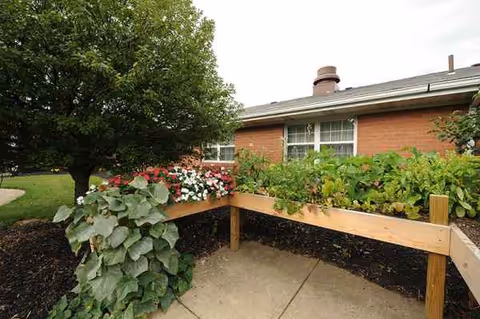 Brick nursing facility exterior with a wooden raised garden bed and blooming flowers.