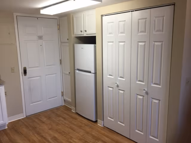 Entry area showing a white front door, a refrigerator between cabinets, and closed bi-fold closet doors on wood flooring.