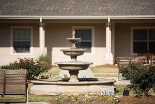Outdoor courtyard area featuring a three-tiered stone fountain surrounded by benches and greenery, with a building facade in the background.