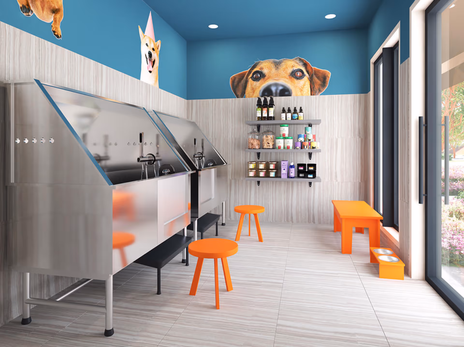 A bright pet washing station with two stainless steel dog wash tubs, orange stools, and a small orange bench with pet food and water bowls. The walls are decorated with large, playful dog murals on a blue upper wall. Shelves with pet care products are mounted on the wall. Large windows let in natural light and show a garden outside.
