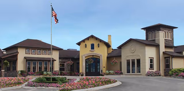 Front view of Villagio of Broomfield senior living facility with flag and landscaped entrance.