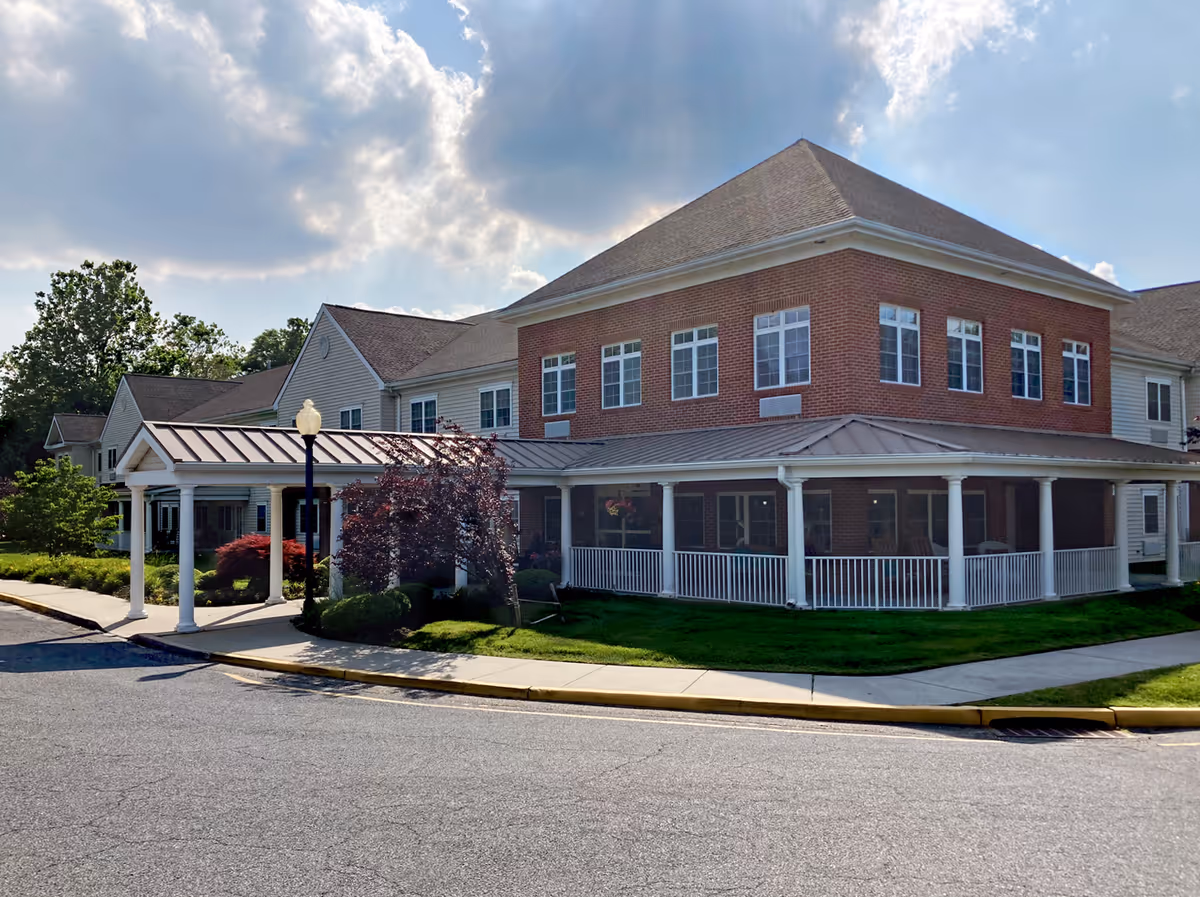 Front exterior of a two-story brick-and-siding senior living facility with a covered entrance and wraparound porch.