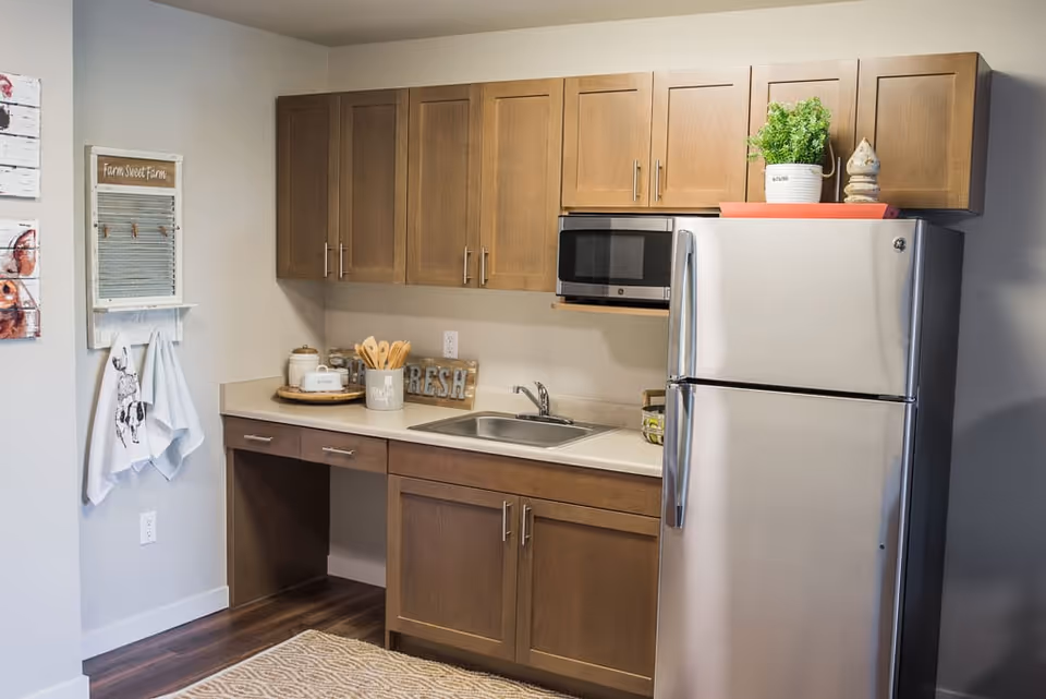 Small kitchenette with wooden cabinets, a stainless steel refrigerator and microwave, a sink, and countertop decor.