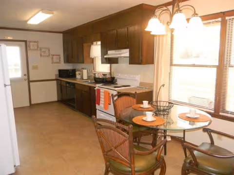 Small kitchen with dark wood cabinets, stove, microwave, and a round glass dining table.