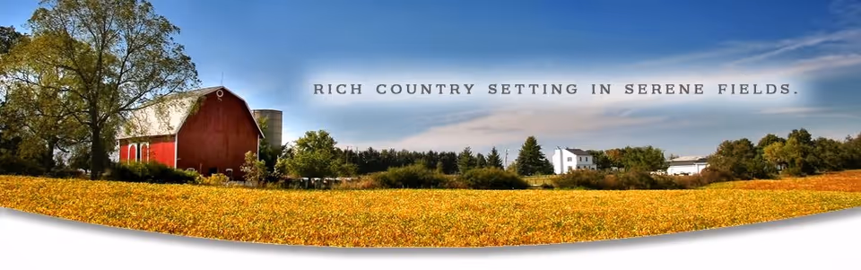 A scenic rural landscape featuring a large red barn, a silo, trees, and a white farmhouse surrounded by expansive golden fields under a blue sky with some clouds.