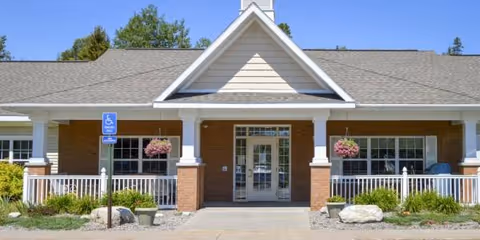 Front exterior of Cedar Cove Assisted Living with entrance, columns, and landscaped shrubs.