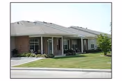 Single-story residential building with a covered porch and several entrances, surrounded by a well-maintained lawn and a paved driveway.