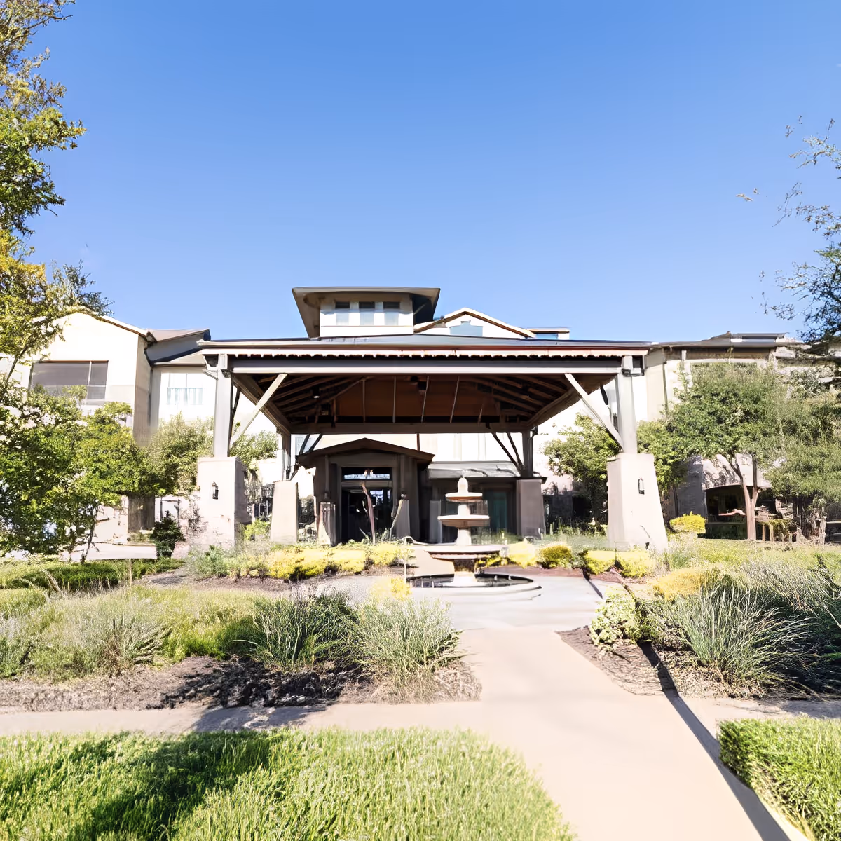 Front entrance of a senior living facility with a covered porte-cochere, central fountain, and landscaped walkway.