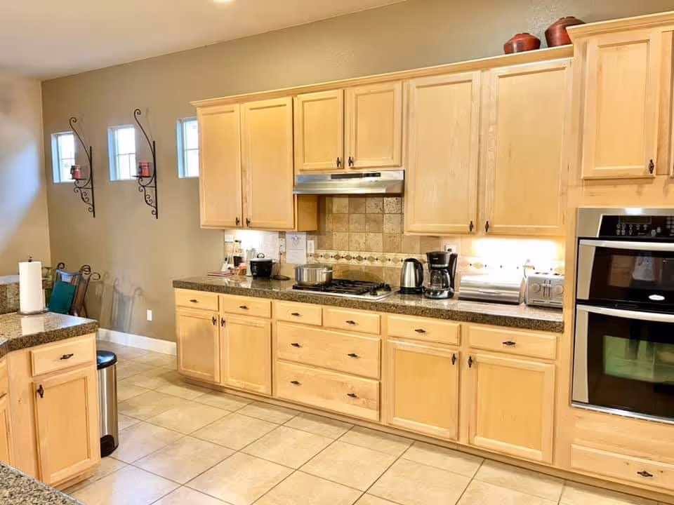 Bright kitchen with light wood cabinets, granite countertops, a stovetop and built-in oven, and small appliances on the counter.