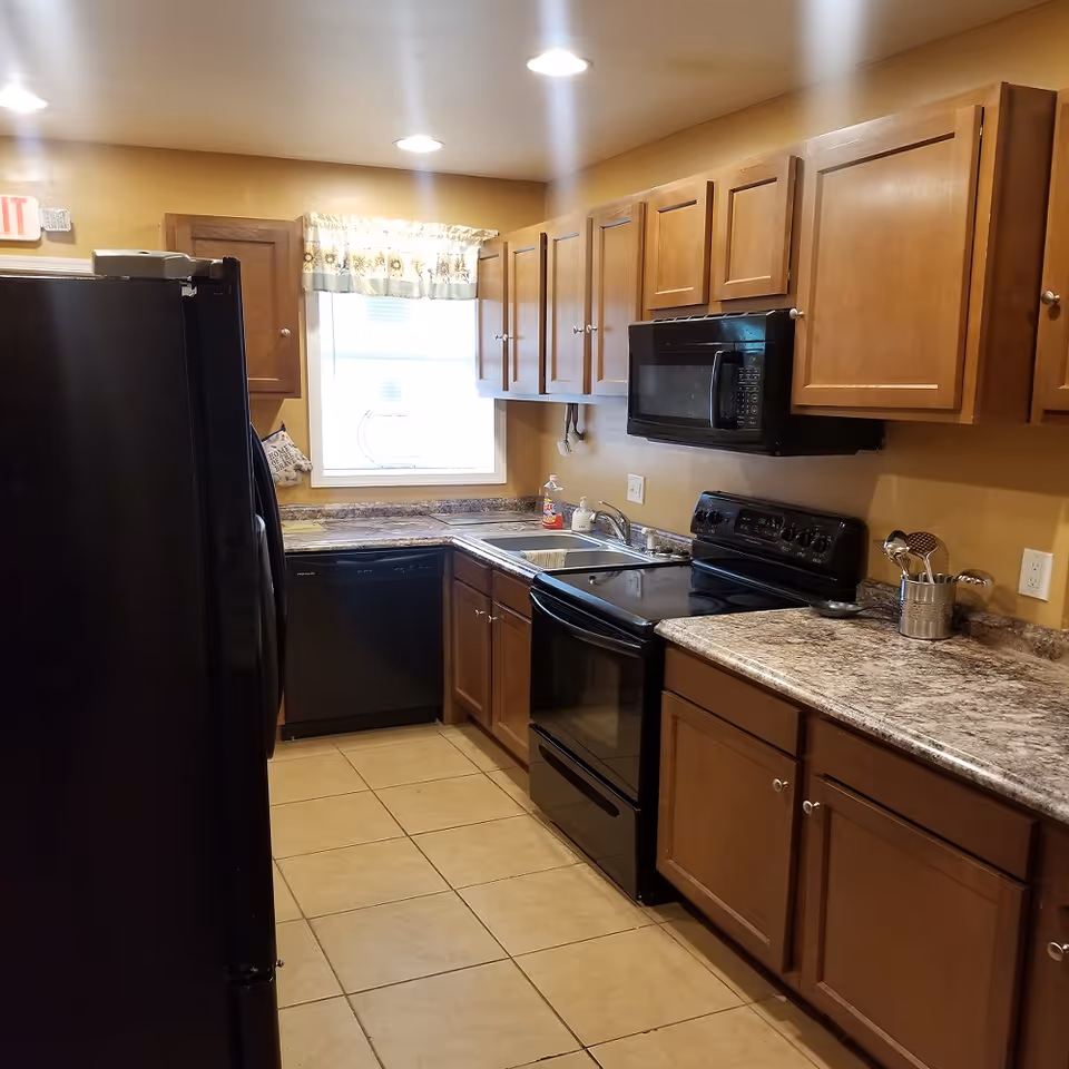 Galley-style kitchen with wooden cabinets, black appliances, and a tiled floor.