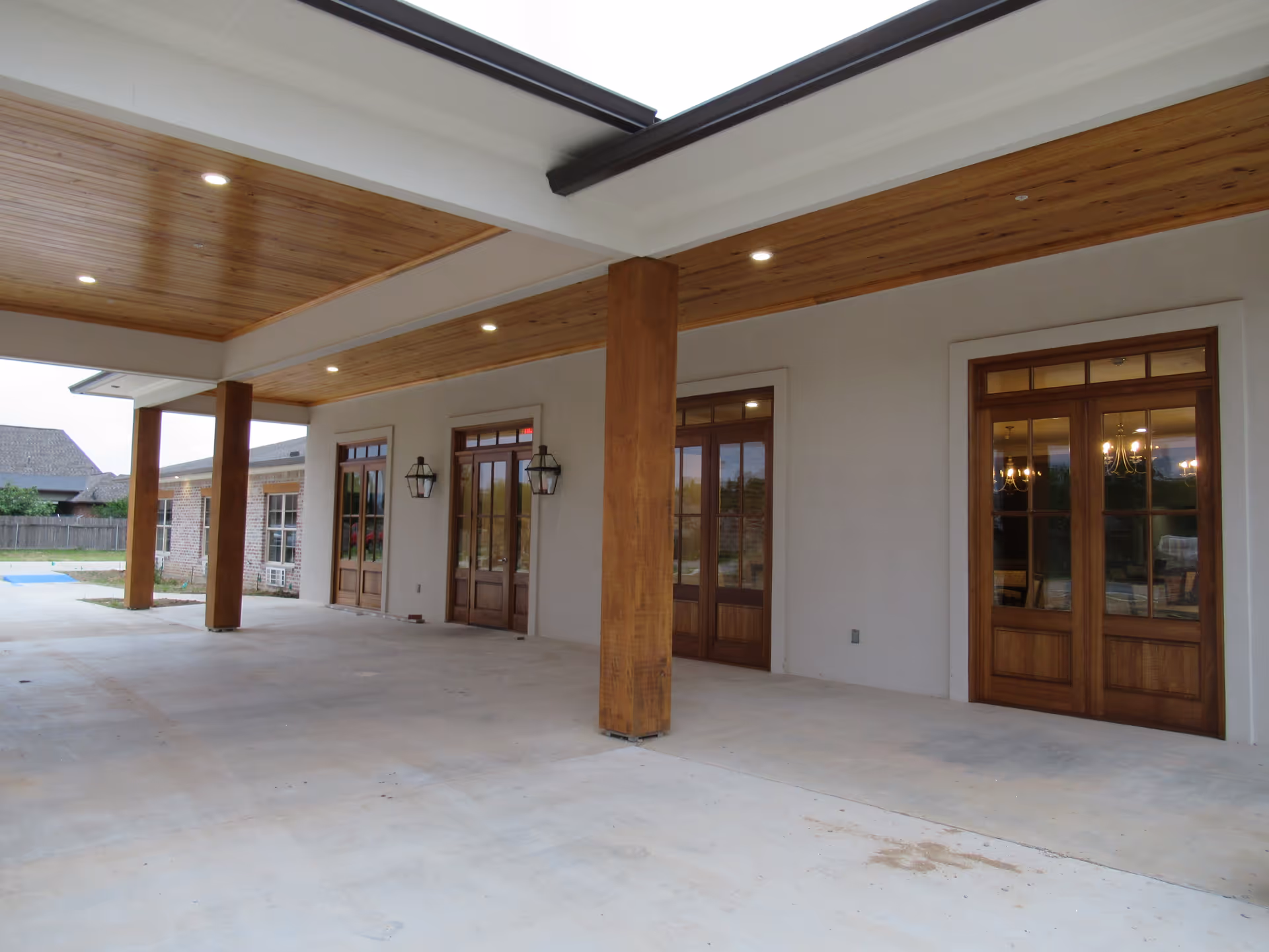 Covered entrance/porch with wooden columns and ceiling, concrete floor, and glass wooden doors with lantern-style lights.