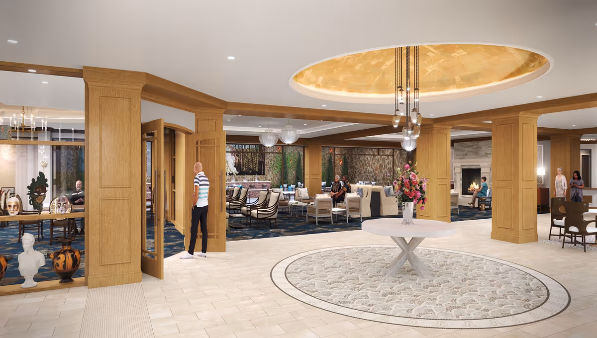 Spacious and elegant senior living facility common area with a round table featuring a flower arrangement in the center, surrounded by wooden columns and a decorative ceiling light fixture. There are multiple seating areas with chairs and sofas, a fireplace, and people engaging in conversation. The floor has a tiled design with a circular patterned rug under the table.