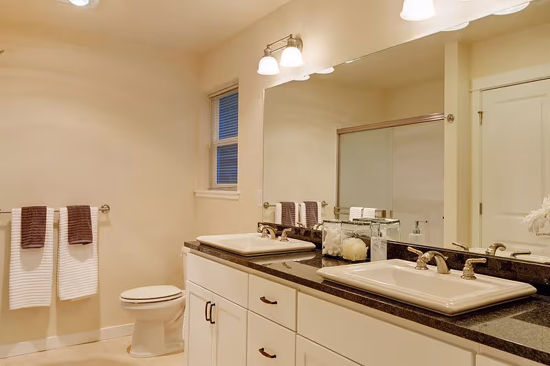 Well-lit bathroom with a double-sink vanity and large mirror, toilet, towel rack, and a sliding-door shower.
