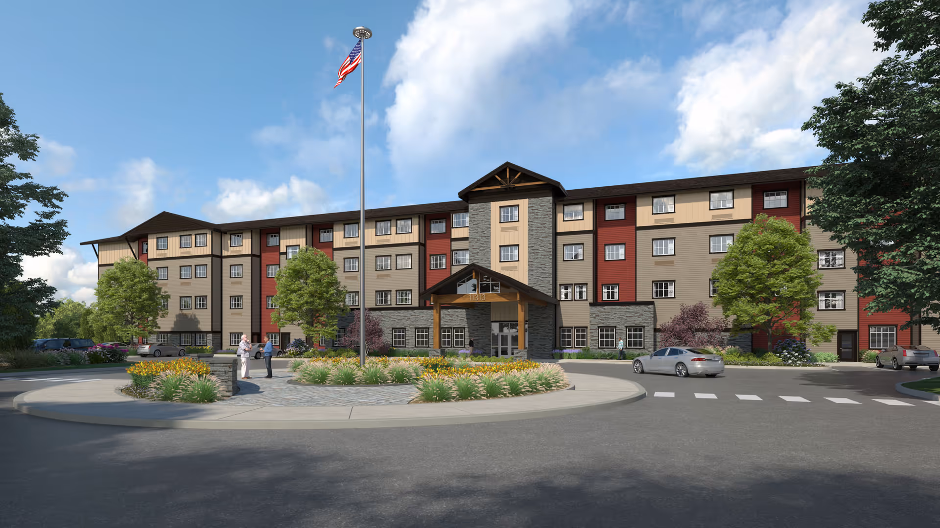 Exterior view of a multi-story senior living facility with a circular driveway, landscaped garden with flowers and shrubs, several trees, an American flag on a tall flagpole, and a few people and cars near the entrance under a clear blue sky.