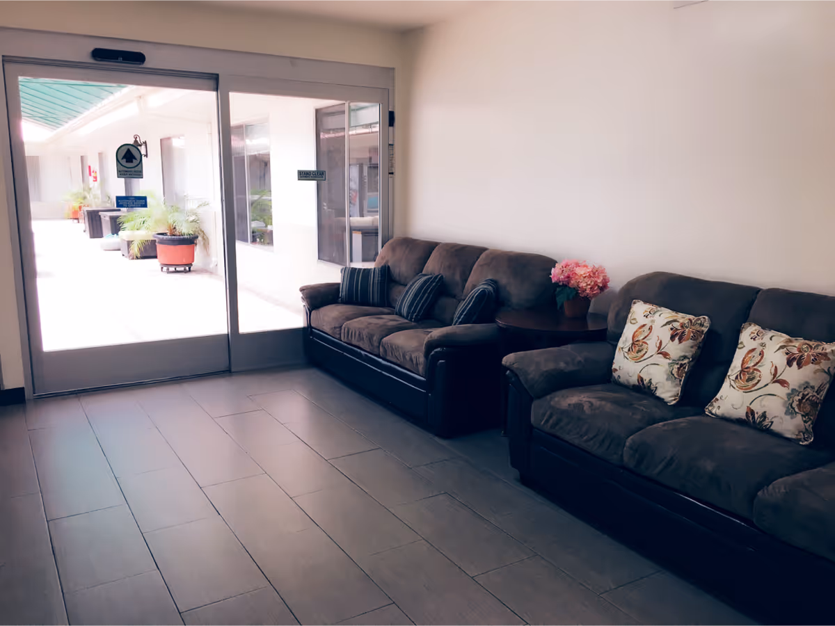 Two sofas with decorative pillows sit along a wall beside glass double doors that open to an outdoor courtyard.