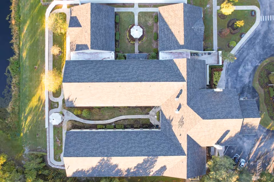 Aerial view of the Madison at Oviedo facility showing the building's roof, surrounding pathways, landscaped gardens, parking area, and nearby water body.