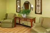 Two beige armchairs sit beside a wooden console with a round mirror and plant.