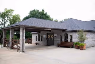 Drive-up covered entrance of a single-story brick building with benches and potted plants under a porte-cochère.