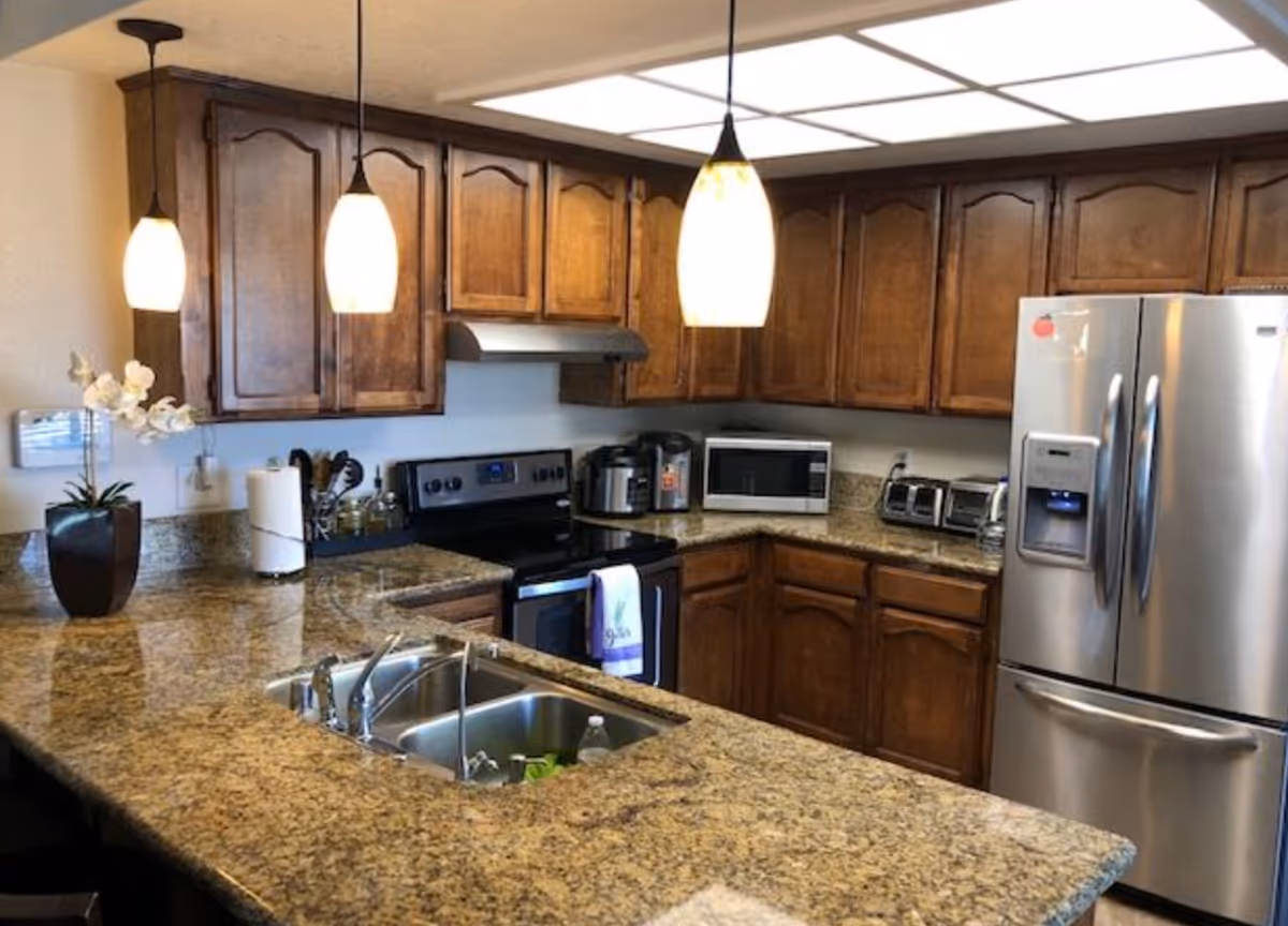 Kitchen with granite countertops, wooden cabinets, stainless steel refrigerator, island sink and pendant lights.