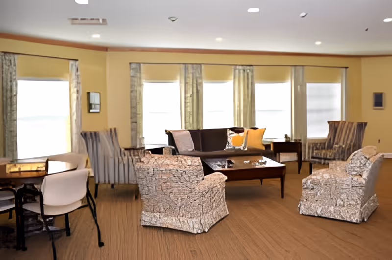 Sunlit communal living room with sofas, armchairs, a coffee table and multiple windows.