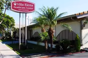 Exterior view of a single-story senior living center with palm trees and a sign.