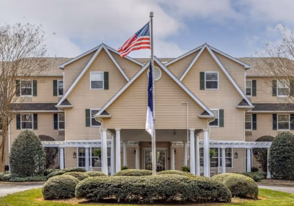 Front view of Lake Wylie Assisted Living and Memory Care building with flags and shrubs.